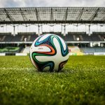 A vibrant soccer ball rests on a lush green field inside an empty stadium, capturing the essence of sports.